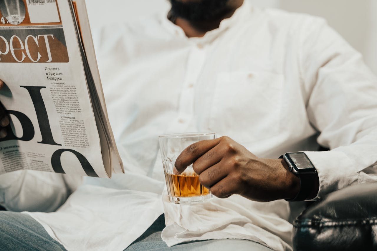 Man reading a newspaper while holding a drink, showcasing leisure and modern lifestyle.